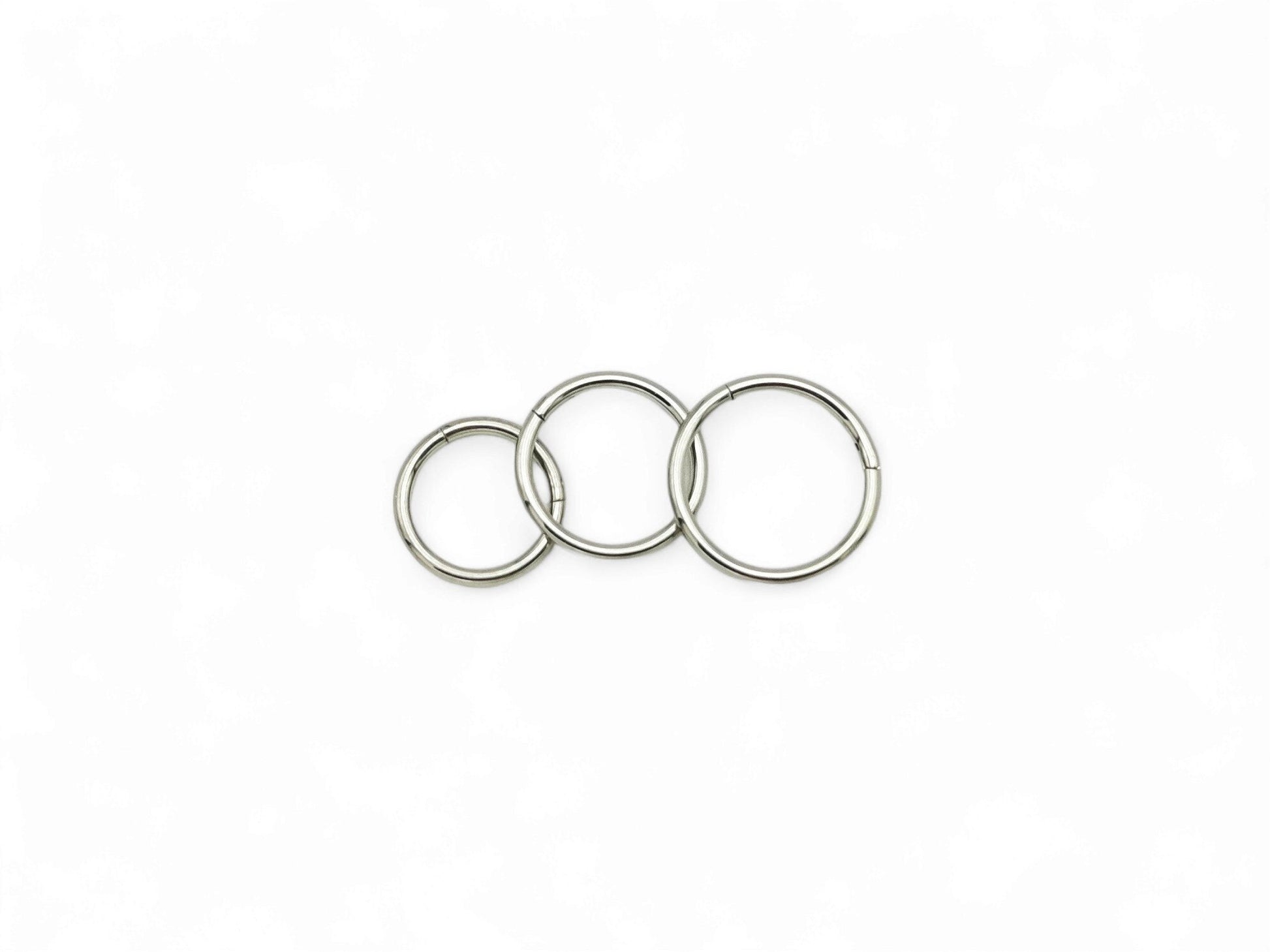 Three overlapping titanium clicker rings with a polished finish, arranged in a stacked configuration against a white background.