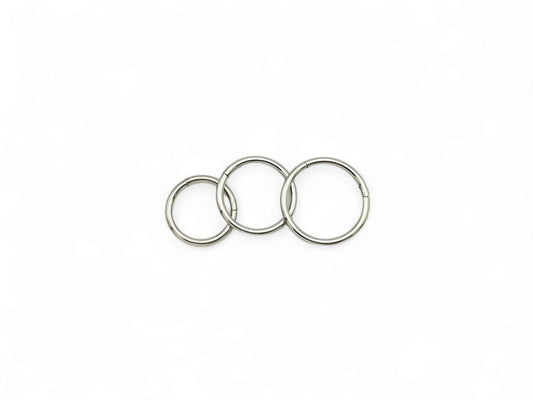 Three overlapping titanium clicker rings with a polished finish, arranged in a stacked configuration against a white background.