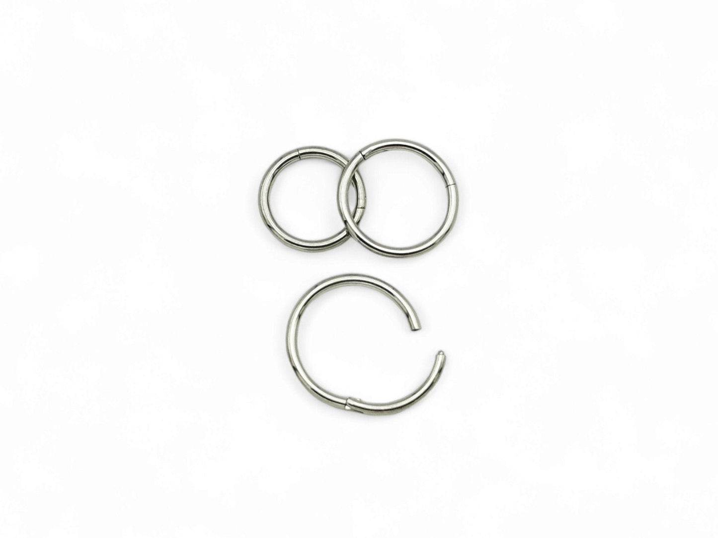 Three overlapping titanium clicker rings with a polished finish, arranged in a stacked configuration against a white background.
