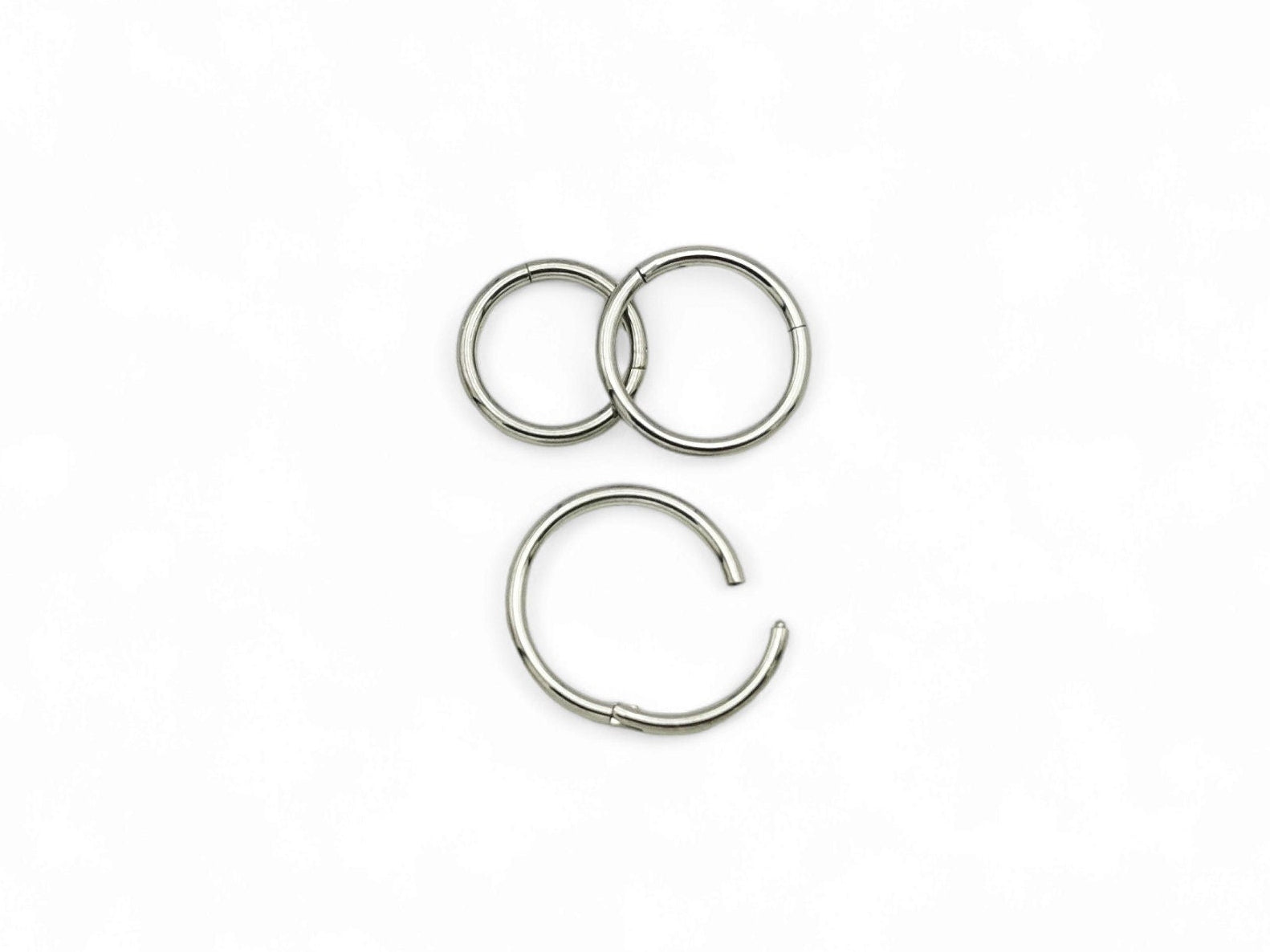 Three overlapping titanium clicker rings with a polished finish, arranged in a stacked configuration against a white background.