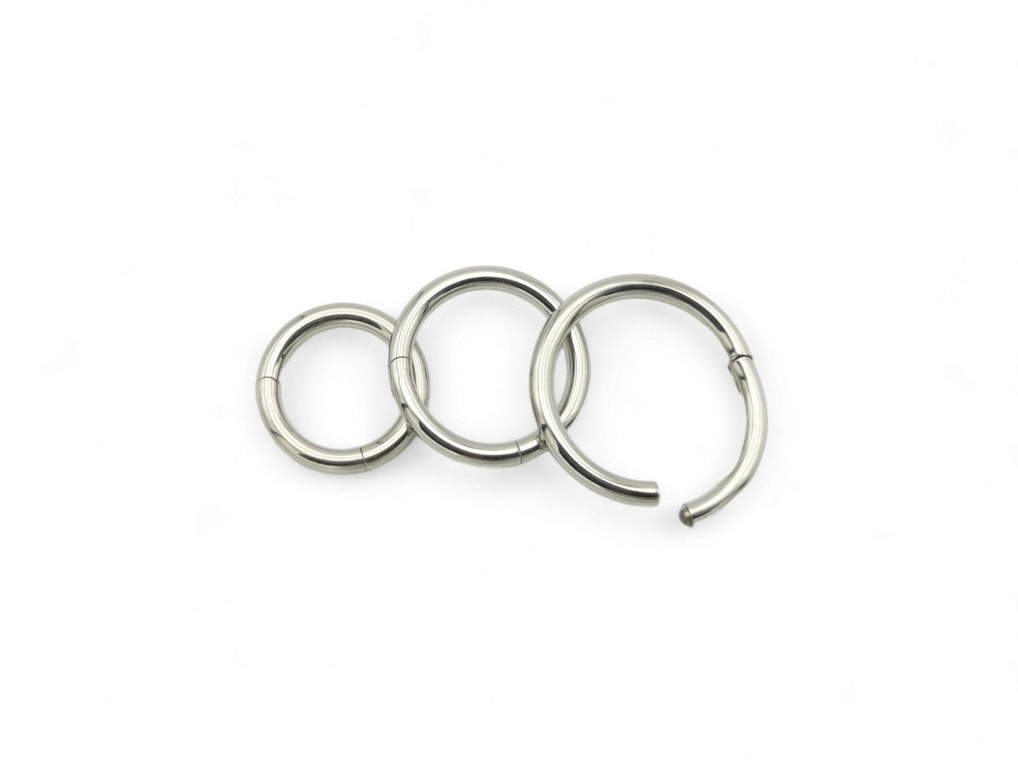 Three polished titanium clicker rings with a silver finish on a white background.