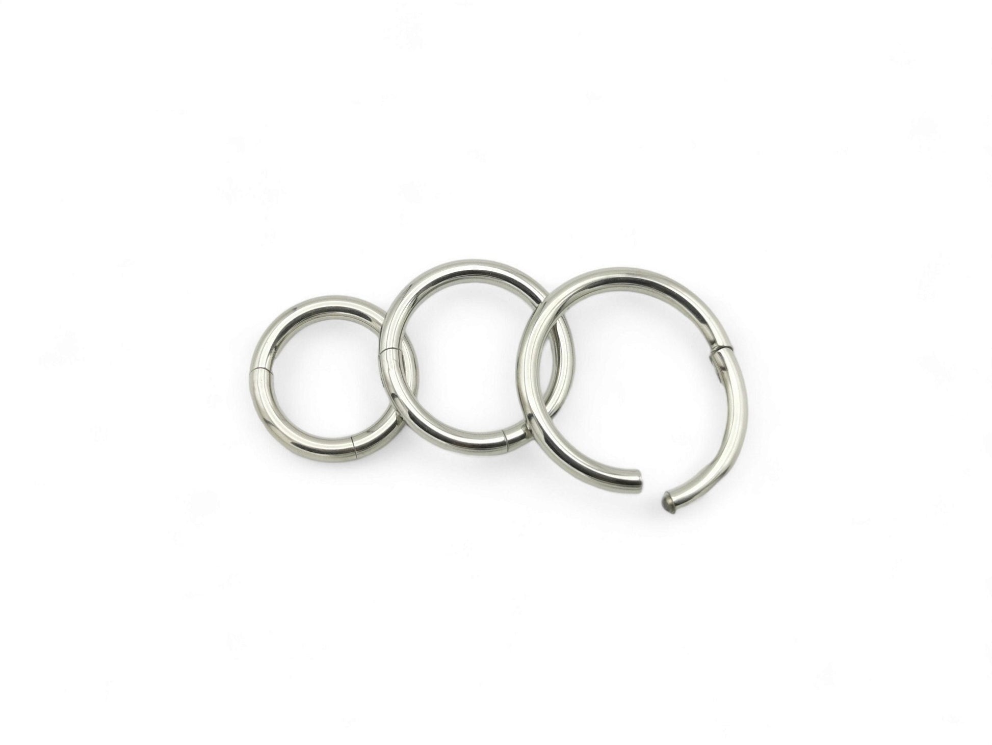 Three polished titanium clicker rings with a silver finish on a white background.