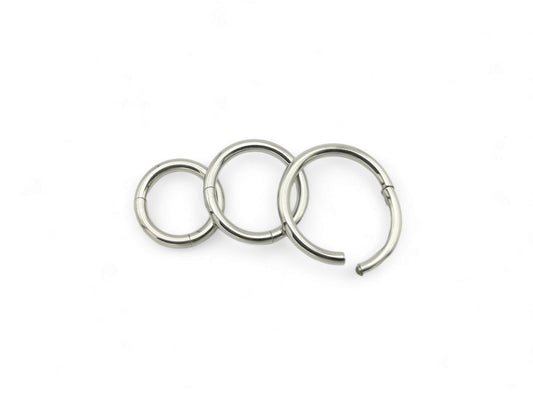 Three polished titanium clicker rings with a silver finish on a white background.