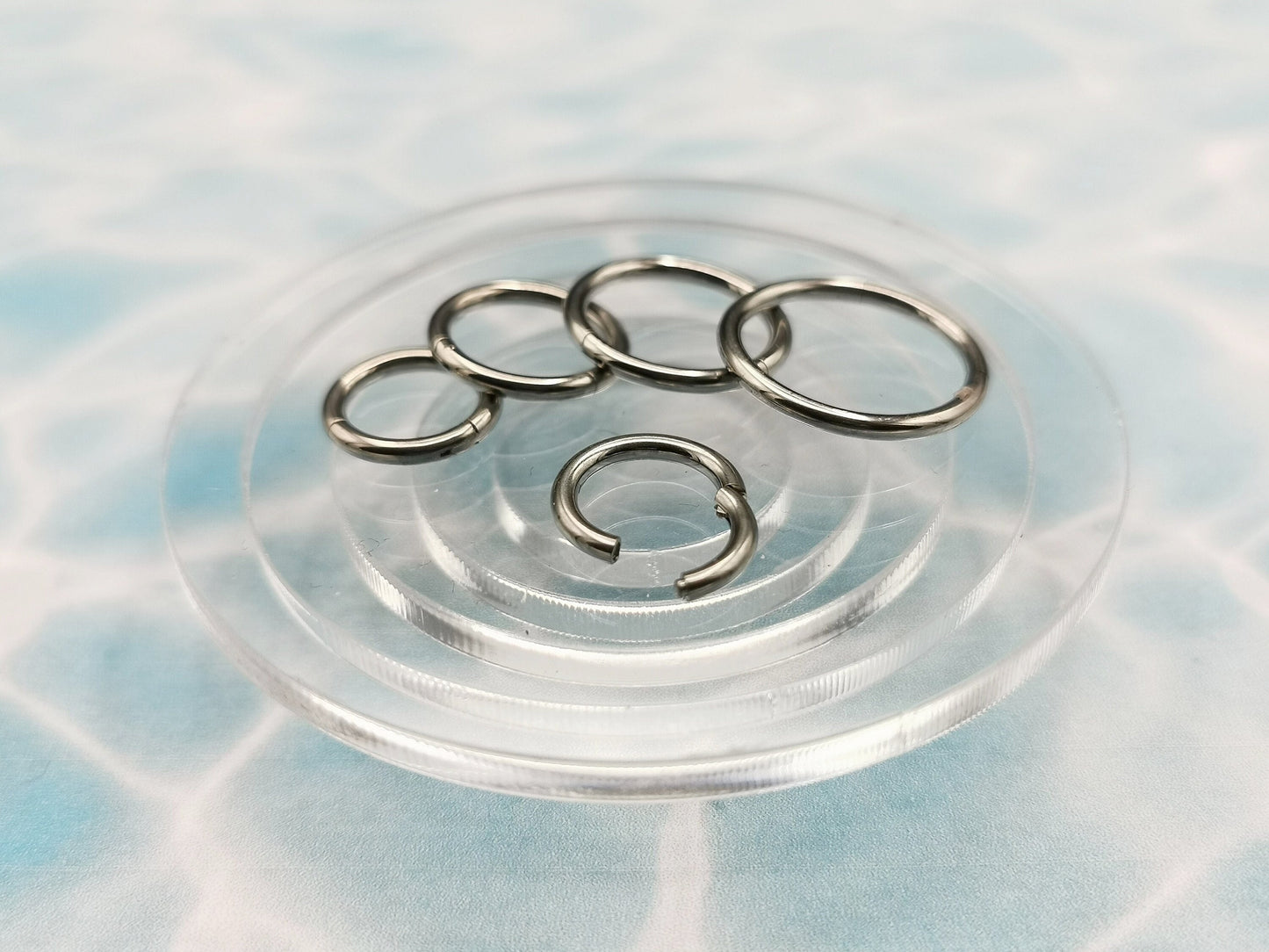 Polished titanium clicker rings with a silver finish on a blue background.