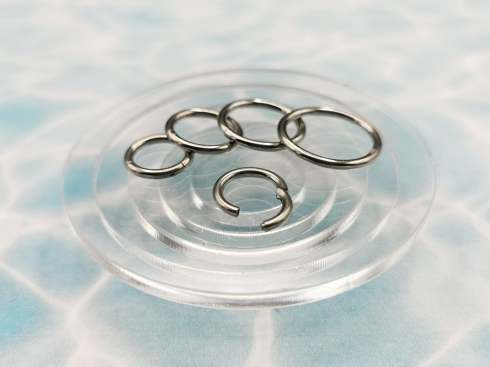 Polished titanium clicker rings with a silver finish on a blue background.