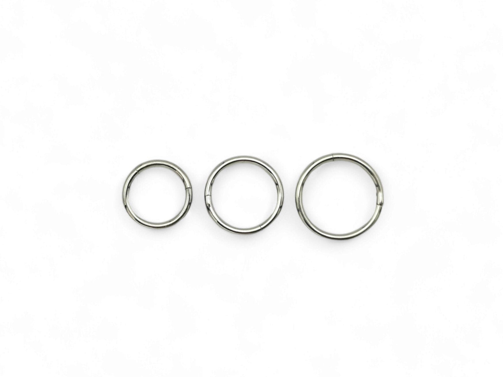 Three overlapping titanium clicker rings with a polished finish, arranged in a stacked configuration against a white background.