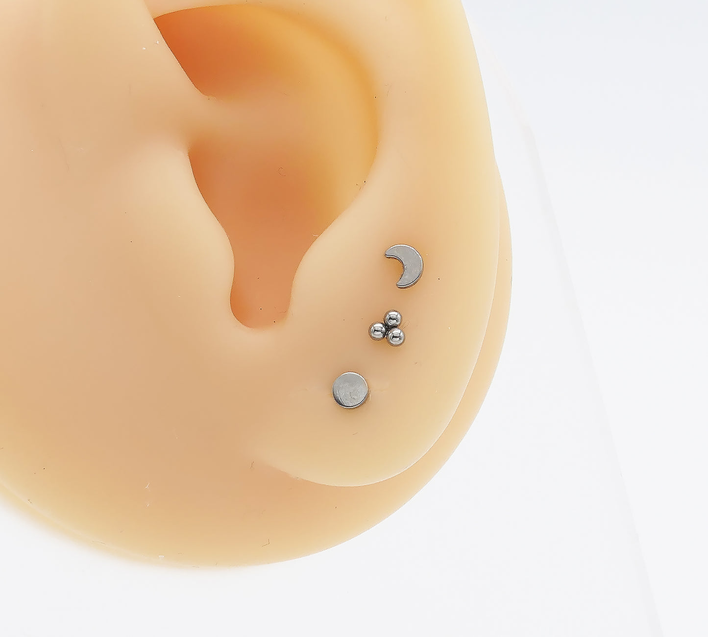 Close-up of an ear with three small silver earrings on a white background
