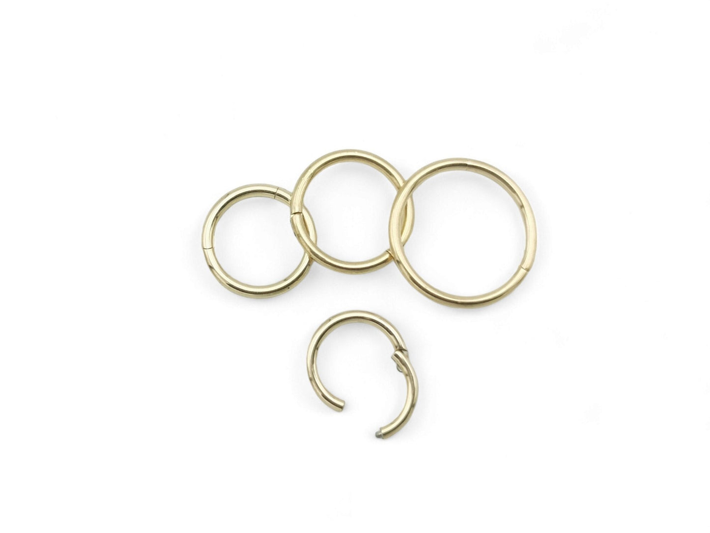 A set of gold-colored titanium clicker rings of different sizes for various body piercings.