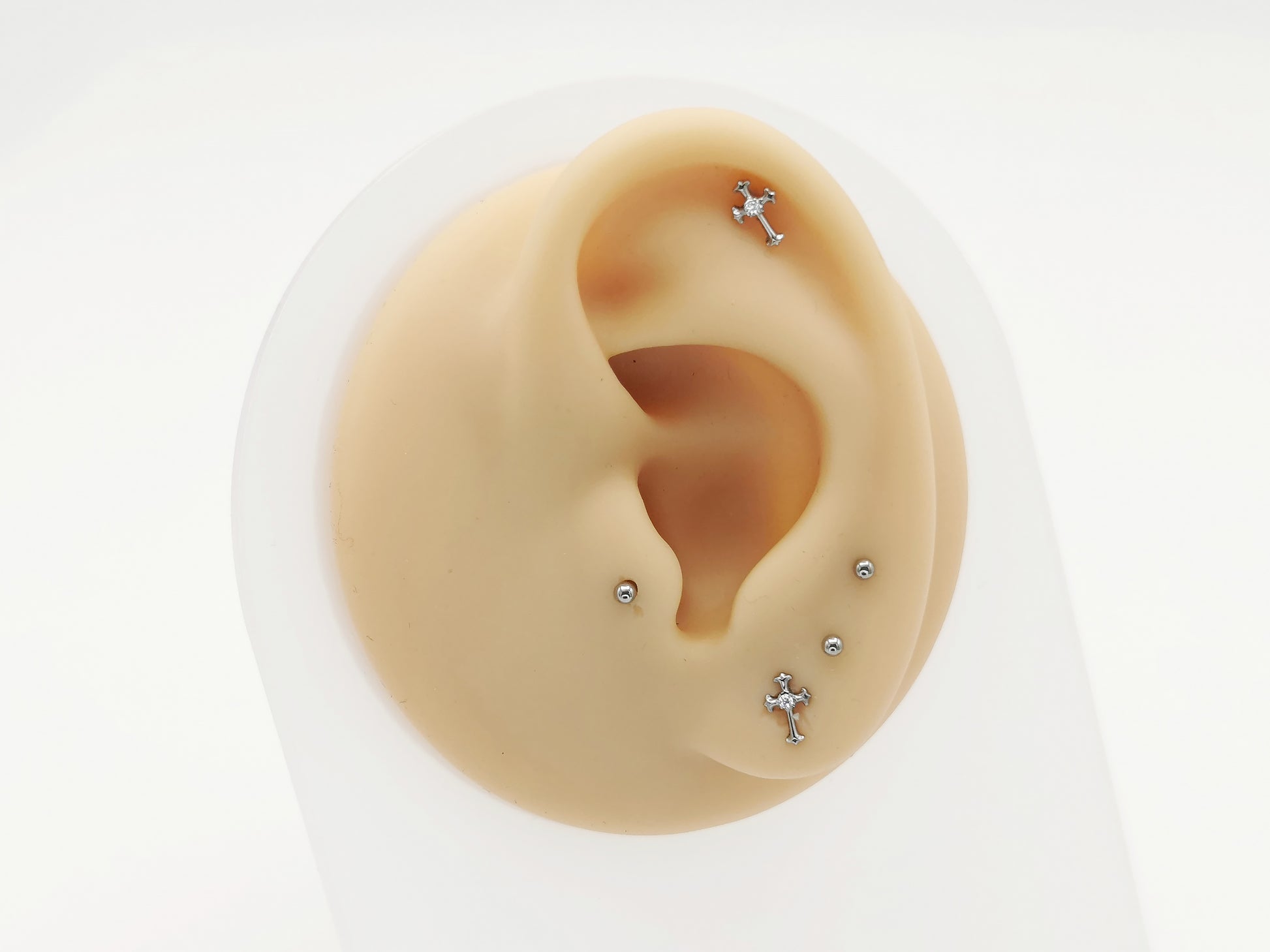 A set of two titanium claw set jewelled crosses with a 1mm clear crystal, polished finish, displayed on a mannequin ear