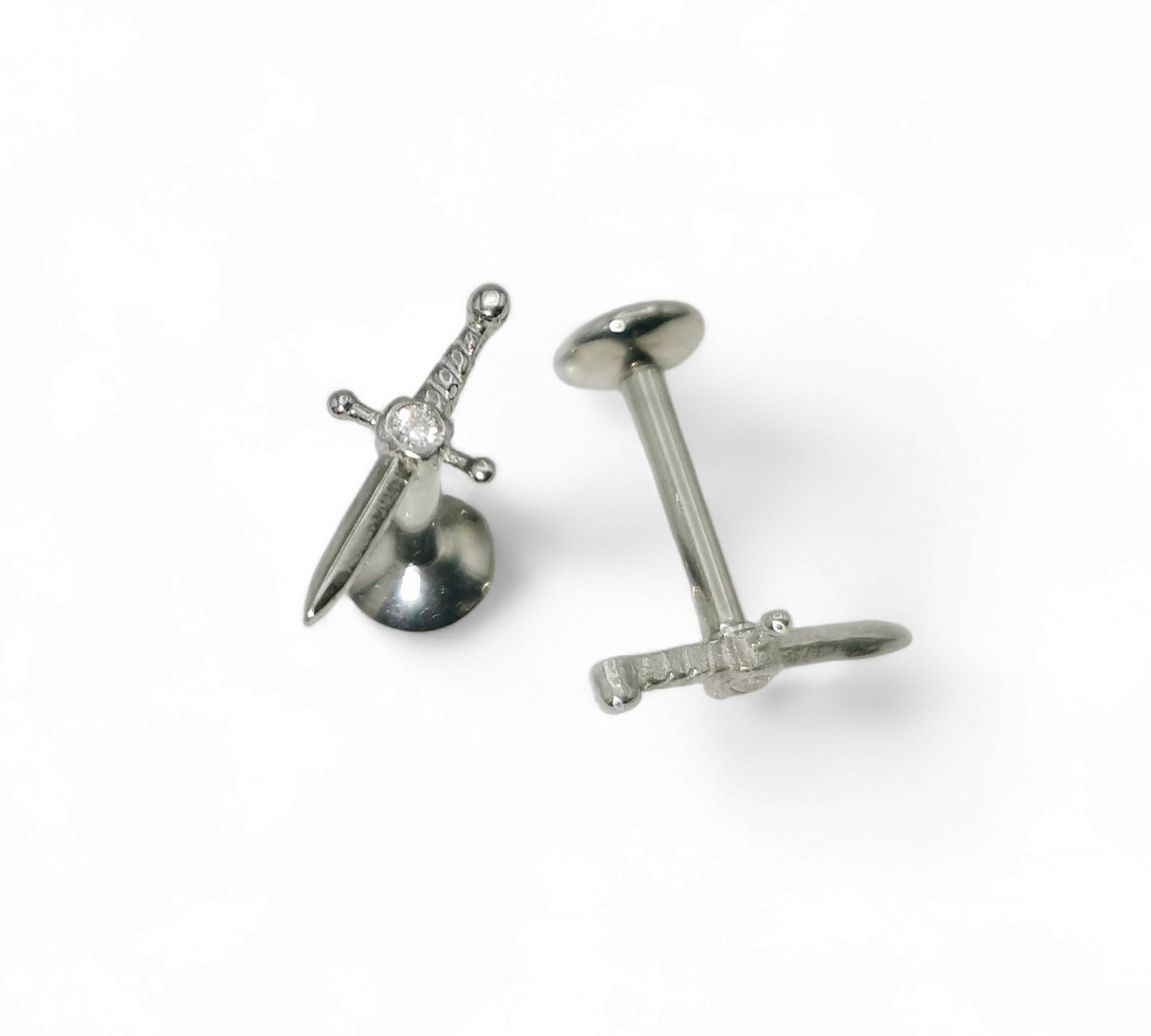 A single silver-colored titanium jewelled dagger stud with a internally threaded post and a sword-shaped top with a gem at the hilt.