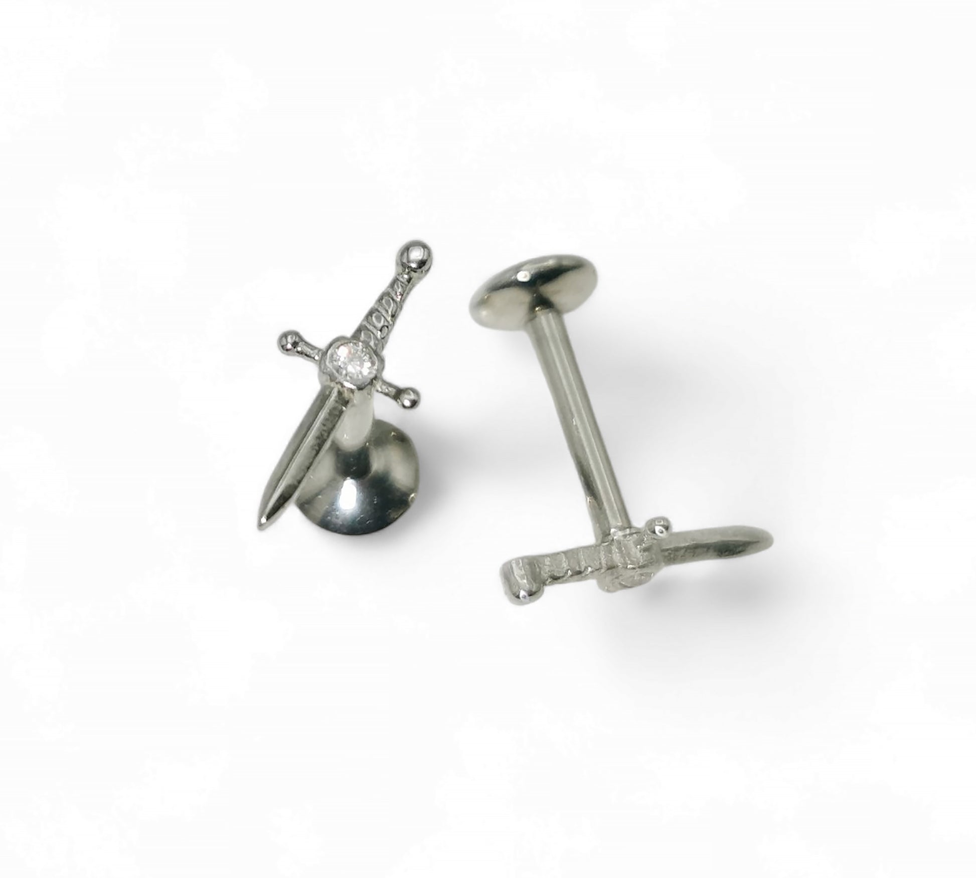 A single silver-colored titanium jewelled dagger stud with a internally threaded post and a sword-shaped top with a gem at the hilt.