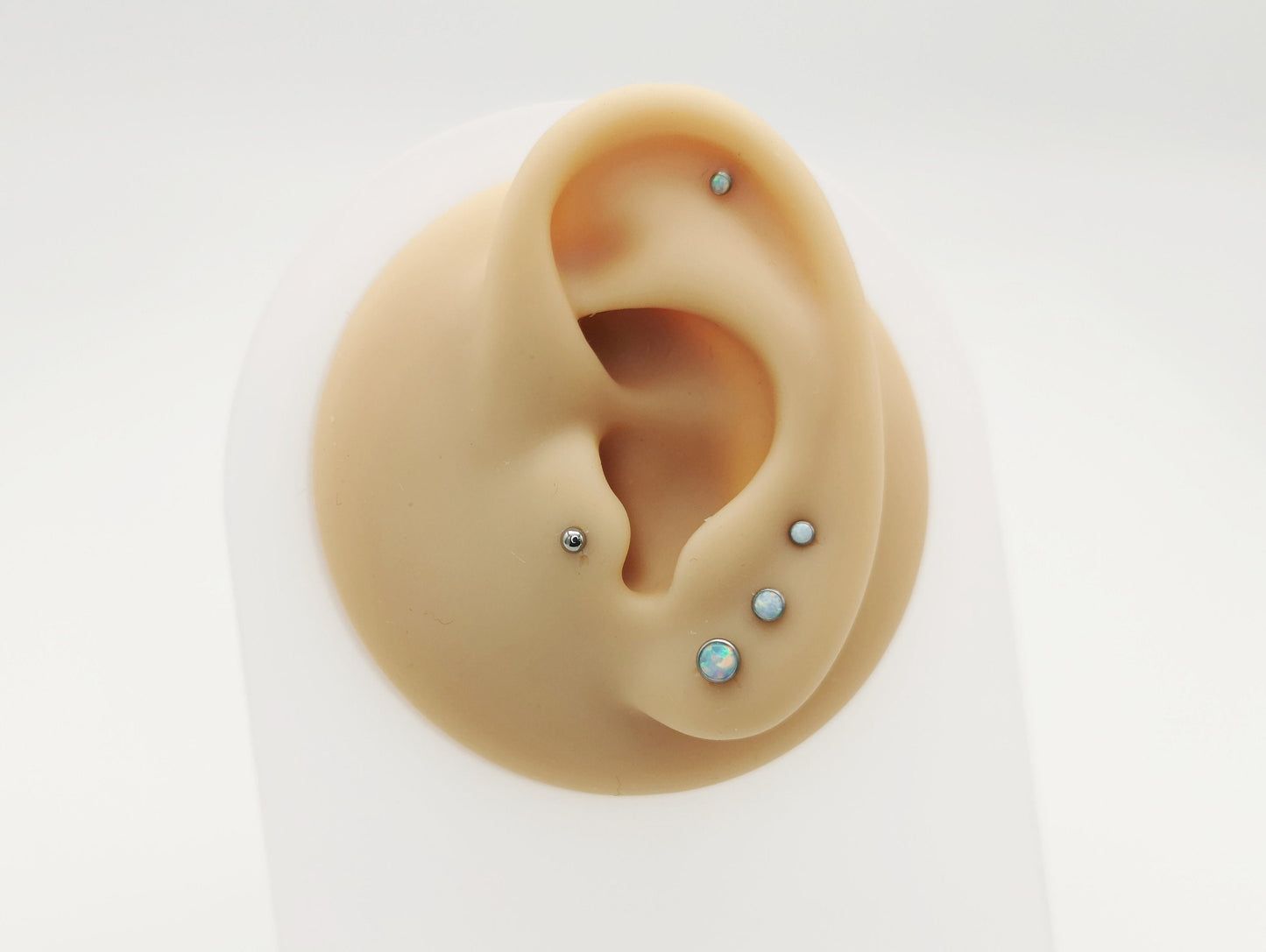 A collection of titanium push-fit stud earrings with bezel-set synthetic opal in various sizes.
