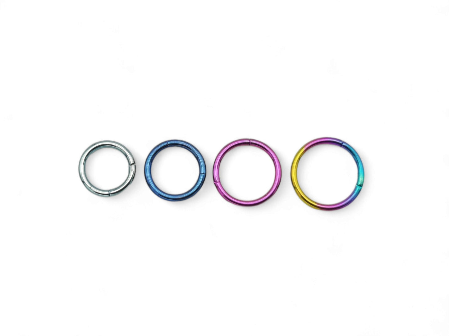 A collection of titanium clicker rings in various colors including polished silver, blue, pink, and multicolored (rainbow). They are designed for use in different types of body piercings.