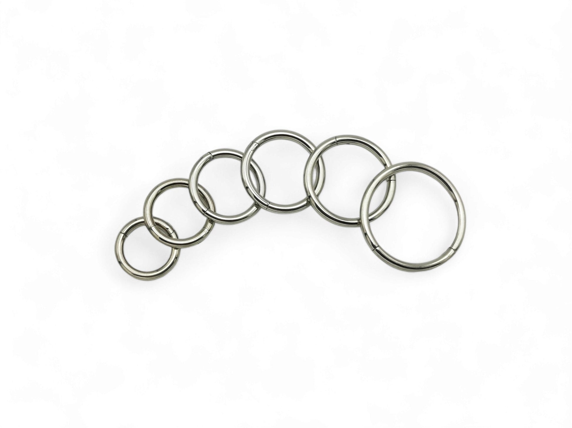 A collection of titanium clicker rings in various colors including polished silver, blue, pink, and multicolored (rainbow). They are designed for use in different types of body piercings.