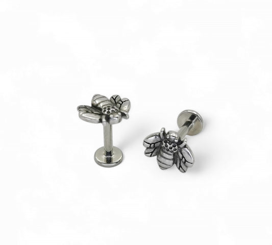 A high-polish finished titanium bee labret stud, with intricate details on the bee's wings and body, on a white background.