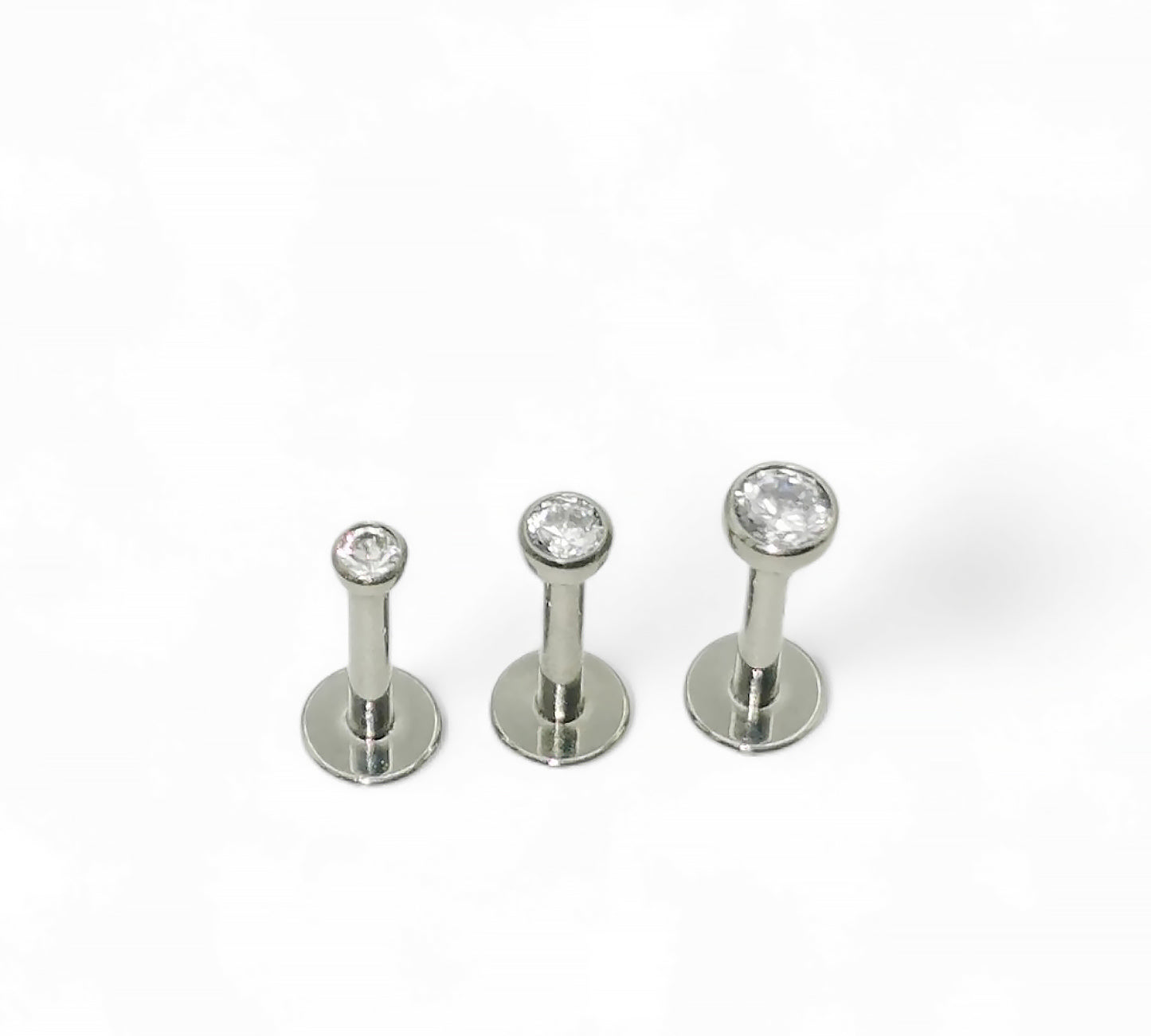 A selection of titanium push fit jewelled studs with bezel-set cubic zirconia in various sizes, displayed against a white background.