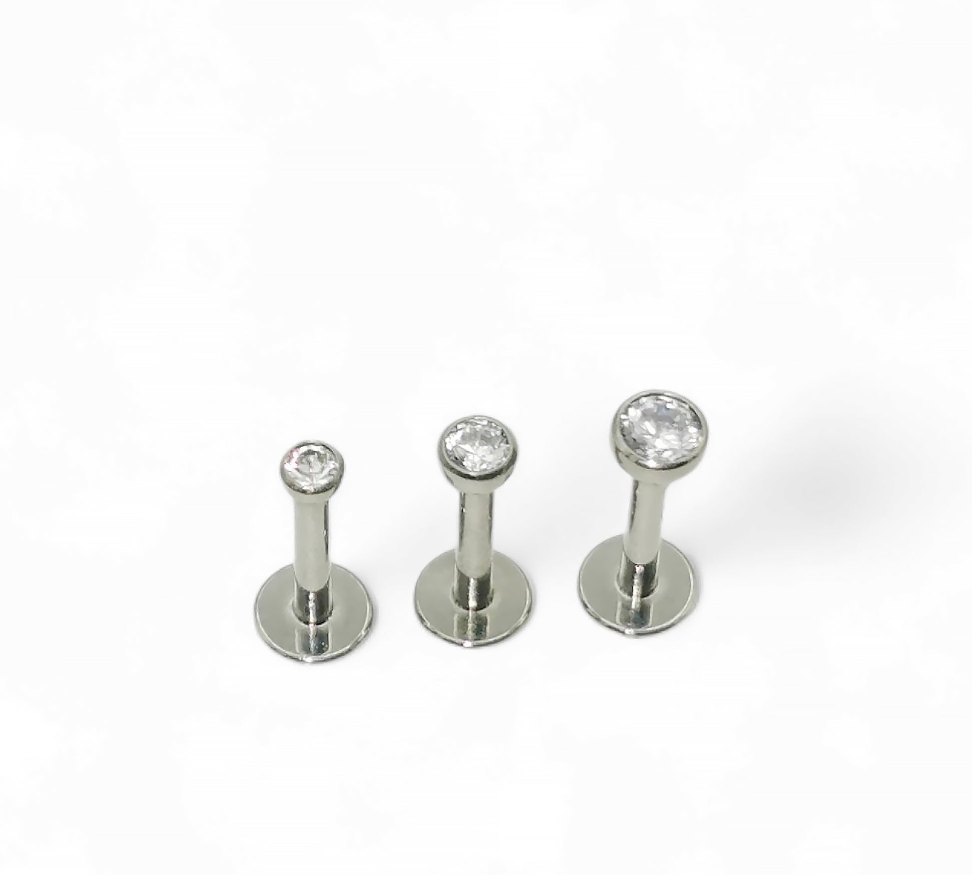 A selection of titanium push fit jewelled studs with bezel-set cubic zirconia in various sizes, displayed against a white background.