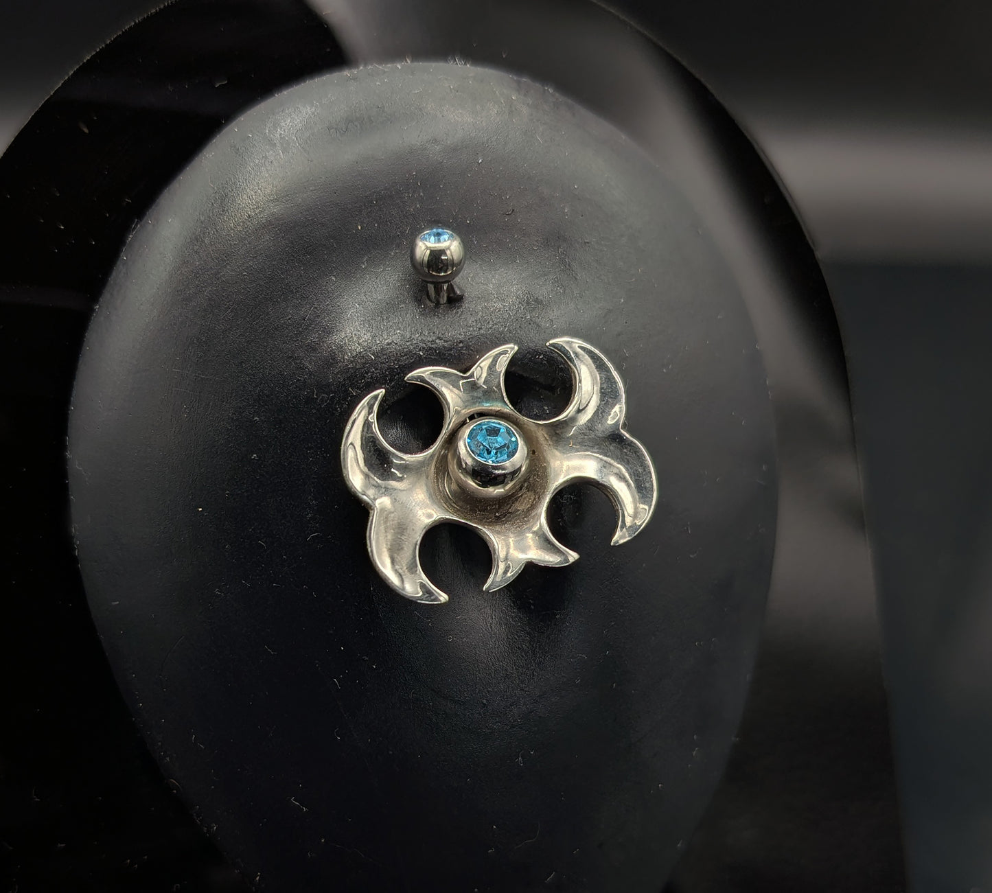 Tribal navel shield with a blue crystal barbell on a dark background