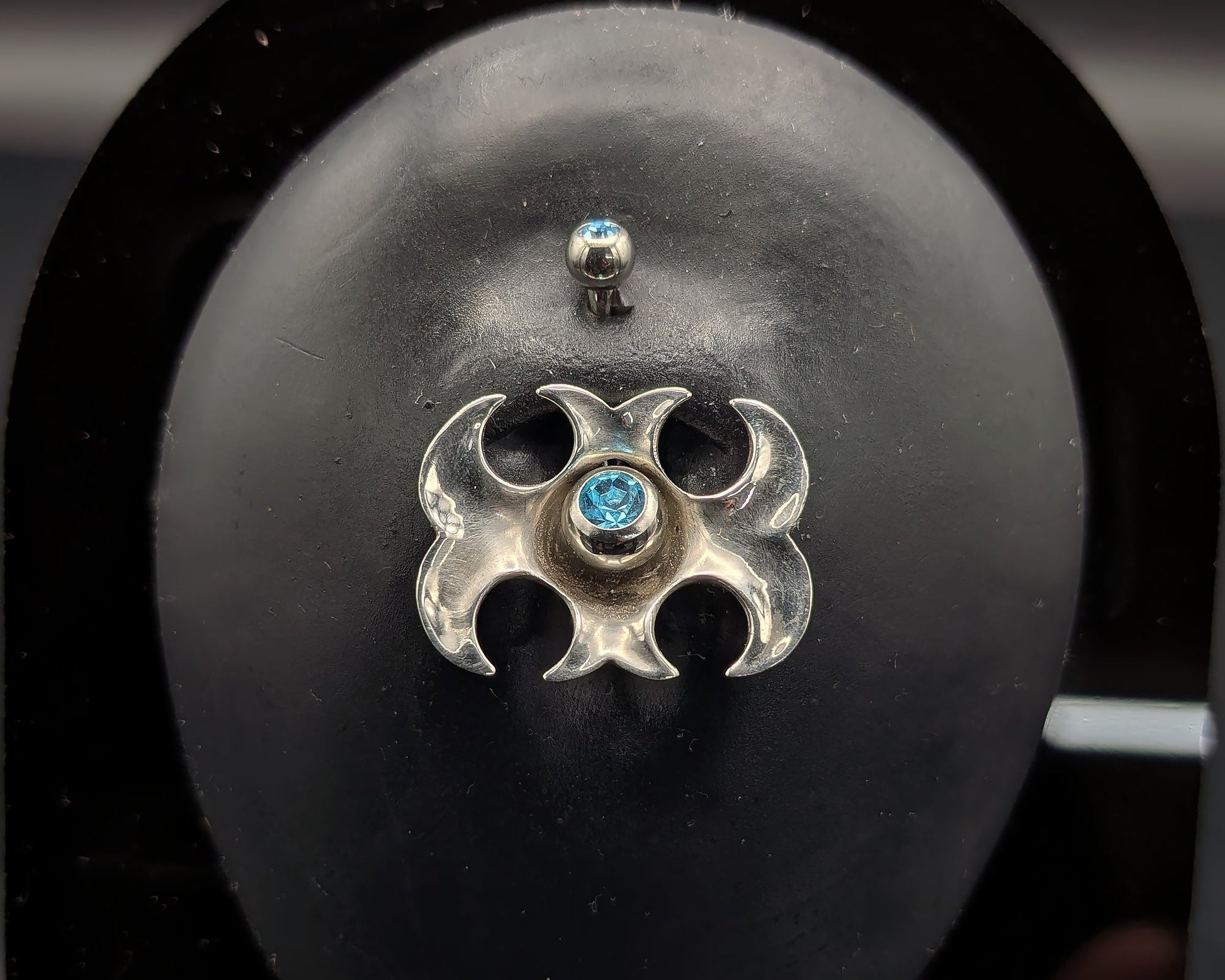Tribal navel shield with a blue crystal barbell on a dark background
