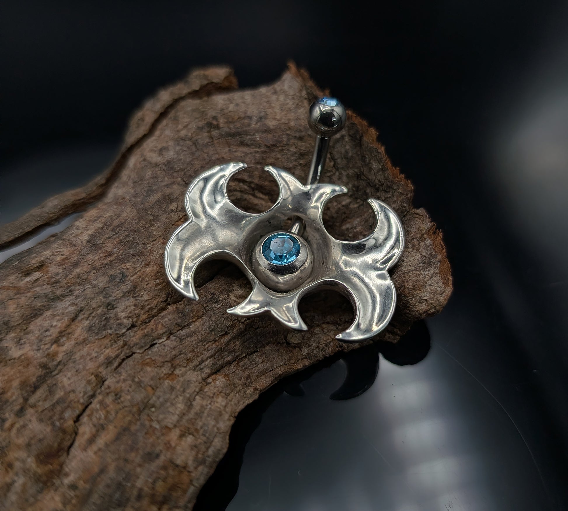Tribal navel shield with a blue crystal barbell on a dark background