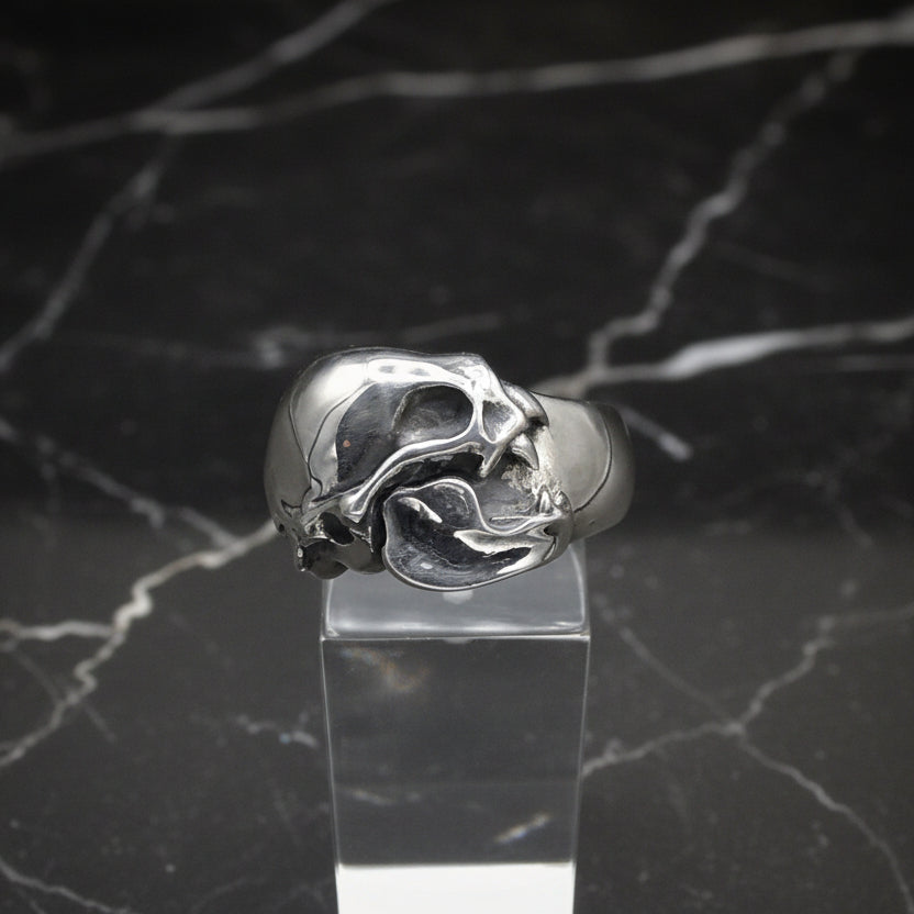 A sterling silver vampire bat skull ring displayed on a clear stand, with a plain grey background.