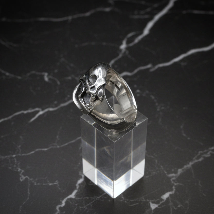A sterling silver vampire bat skull ring displayed on a clear stand, with a plain grey background.